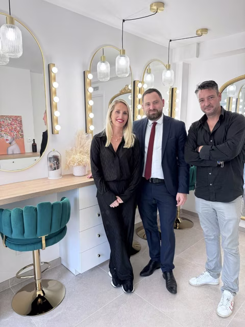 Jennifer Perseverante, accompagnée de Jonathan Wofsy, le Maire de Chevry-Cossigny, et d'Alexandre Chevalier, adjoint en charge de la vie économique, dans son élégant studio de maquillage. Le trio est entouré d'un décor sophistiqué, avec des miroirs illuminés et des tabourets en velours vert
