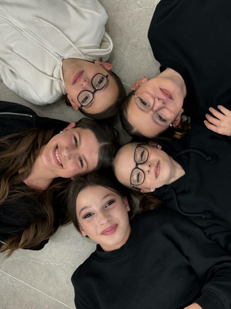 Cinq jeunes filles allongées en cercle, leurs visages souriants tournés vers l’objectif. Une belle mise en scène dans un moment complice, capturé dans l’ambiance chaleureuse d’un atelier maquillage