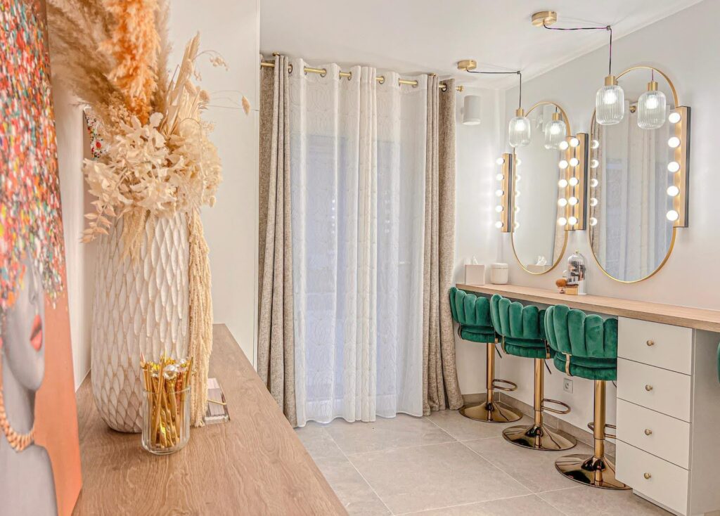 Un élégant atelier de maquillage à la décoration raffinée, avec des fauteuils verts en velours, des miroirs illuminés et des touches dorées. Une ambiance chic et moderne, parfaite pour des moments de beauté et de détente